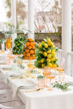 the table is set with oranges, lemons and greenery in glass vases