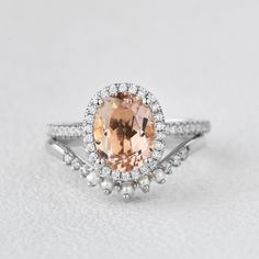 an oval shaped peach morganite and diamond ring on a white surface with pearls around the band