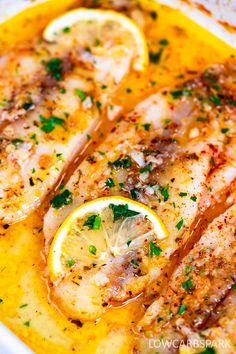 fish with lemons and parsley in a yellow sauce on a white platter