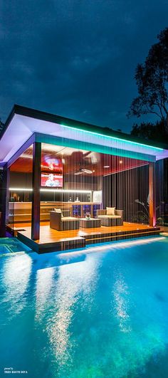 an outdoor swimming pool at night with the lights on and curtains hanging from the ceiling