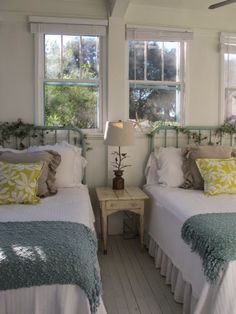 two beds in a room with white walls and wooden floors, one has green pillows on it