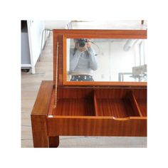 a person taking a photo in a mirror on a wooden desk with drawers underneath it