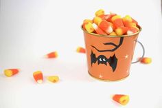 an orange bucket filled with candy corn on top of a white table next to other candies