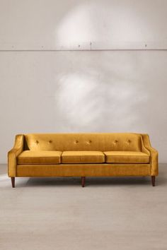 a yellow couch sitting on top of a cement floor next to a white brick wall