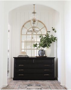 a black dresser with mirror and potted plant on top in front of arched doorway