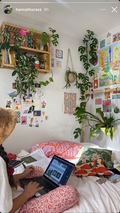 a person sitting on a bed with a laptop computer in front of them and some plants