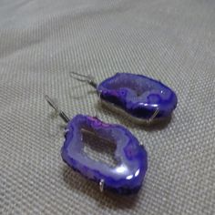 two purple earrings sitting on top of a bed