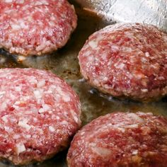 four hamburger patties cooking in a frying pan