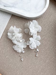 two white flowers sitting on top of a piece of cloth next to a tray with an object in the background