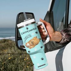 a person holding a coffee cup in front of a car with a cat on it