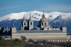 a large building with two towers and snow covered mountains in the background