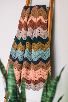 a crocheted blanket hanging on a ladder next to a potted plant