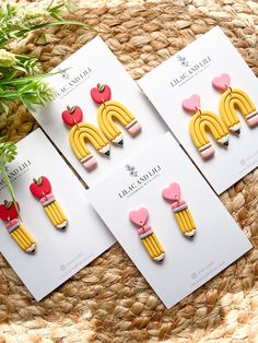 three pairs of yellow and pink earrings on top of a woven basket next to a plant