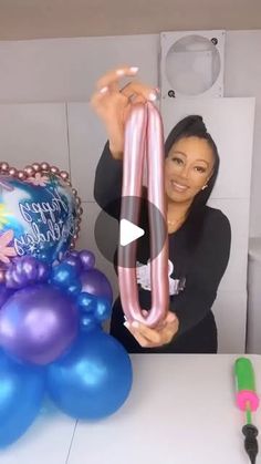 a woman holding up a pink balloon in front of balloons and streamers on a table