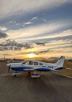 a small plane sitting on top of an airport tarmac at sunset with the sun in the background