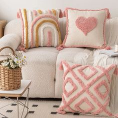 a white couch with pink and yellow pillows on it's back, next to a wicker basket filled with flowers