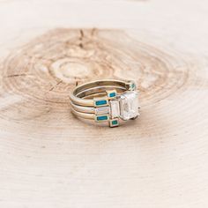 two gold rings with blue and white stones on top of each other in front of a tree stump