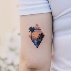 a woman's arm with a palm tree and sunset tattoo on the left side of her arm