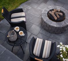 two chairs sitting next to each other on top of a stone patio near a fire pit