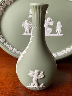 a green vase sitting on top of a wooden table next to two plates with angels painted on them