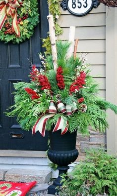 a black vase with red and white flowers in front of a door decorated for christmas