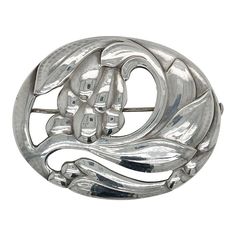 A fine antique Georg Jensen brooch or pin.  In sterling silver.  Model no. 65 with a floral motif.  Designed by Georg Jensen.  Together with its original box from Walter Muhke-Hofjuwelier Coblenz (Crown Jeweler).  Simply a wonderful brooch from one of Denmark's premier silversmiths!  Date: Early 20th Century  Overall Condition: It is in overall good, as-pictured, used estate condition.  Condition Details: There are two small spots of persistent tarnish to the reverse of the brooch. Otherwise, th Classic Silver Brooches With Intricate Design, Vintage White Gold Oval Brooches, Silver Art Nouveau Brooches As Gift, Silver Art Nouveau Brooches For Gifts, Silver Engraved Brooches For Formal Occasions, Classic Oval Silver Brooches, Silver Art Nouveau Brooch, Antique Silver Brooch, Antique Silver Hallmarked Brooches