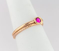 Crafted by hand with meticulous care and featuring a rich fuchsia cubic zirconia stone in a gold-filled bezel, these dainty hot pink and gold stacking rings are luxurious and timeless. The bold contrast of the bright gold bands and the deep pink hue of the pink gemstone creates an elegant and regal color combination that is sure to inspire. With a modern twist in the form of a gold-filled arrow accent, these Pink Gemstone Rings are a must-have addition to any outfit, whether for everyday wear or Pink Ruby Stackable Jewelry, Pink Ruby Birthstone Ring In 14k Gold, 14k Gold Pink Ruby Ring Birthstone, Gold Ruby Solitaire Birthstone Ring, Gold Ruby Birthstone Ring With Solitaire, Pink Birthstone Ring With Round Band, Rose Gold Stackable Rings With Pink Sapphire As Gift, Pink 14k Gold Stackable Rings For Anniversary, Rose Gold Pink Sapphire Stackable Rings As Gift