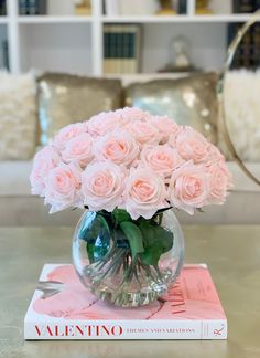 a vase filled with pink roses sitting on top of a table next to a book