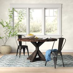 a dining table with two chairs and a potted plant on the rug in front of it