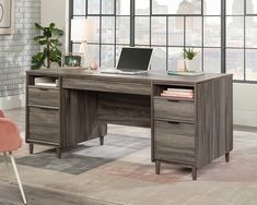 an office desk with a laptop on it in front of a window and a chair