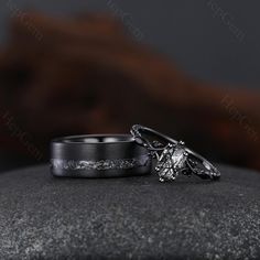 two wedding rings sitting on top of a rock in front of a dark background with an intricate design