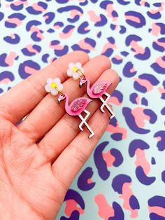 a hand holding three pink flamingo shaped earrings