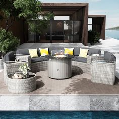 an outdoor living area with grey wicker furniture and yellow pillows on the floor next to a body of water