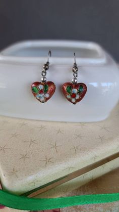 These are a very pretty pair of vintage dangling cloisonne heart shaped earrings. Unsigned. A few light surface scratches and some minor discoloration consistent with age. Please see photos. Sold as is. Priced accordingly. Will be packaged in a gift box perfect for giving. I will refund any shipping overages. Does not include any props in photos. Please feel free to contact me with any questions you may have. Before you buy, please note that the items in my shop are pre-owned and may (or may not Vintage Heart Charm Earrings For Valentine's Day, Heart Charm Enamel Earrings, Heart-shaped Enamel Earrings With Charm, Vintage Pierced Enamel Earrings, Handmade Heart-shaped Enamel Earrings, Vintage Heart Charm Drop Earrings, Vintage Nickel-free Earrings For Valentine's Day, Nickel Free Vintage Earrings For Valentine's Day, Vintage Drop Earrings For Valentine's Day