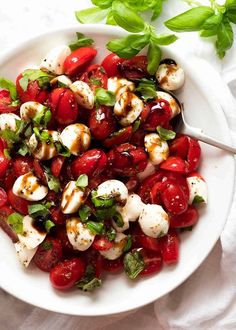 a white bowl filled with tomatoes and mozzarella on top of a white table