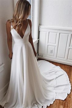 a woman in a white wedding dress standing by a window with her back to the camera