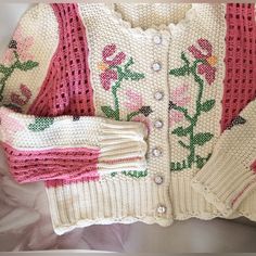 a white sweater with pink and green flowers on it, next to a pair of gloves