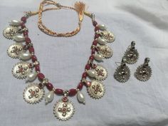 * This classic piece of craft is embellished with various elements in a true traditional kuchi style. The vintage coins and beads, adding a contrast of vibrant reddish maroon and rustic gold hues. The handcrafted set includes a necklace, a pair of earrings, and a ring. * The astonishing necklace is crafted in an ancestral vintage style of mala with dangling golden antique coins along with stones and beads. Each coin embellished with finely carved archaic stamp. The identical coins are used for t Traditional Jewelry With Motifs For Navratri, Beaded Jewelry For Rituals And Festivals, Handmade Jewelry For Rituals And Festive Occasions, Handmade Jewelry For Rituals And Festive Season, Artisan Silver Beads Jewelry For Festivals, Handmade Kundan Bohemian Earrings, Artisan Silver Beads Jewelry For Festive Occasion, Red Motif Jewelry For Rituals, Handmade Bohemian Kundan Earrings