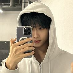 a young man taking a selfie with his cell phone while wearing a white hoodie