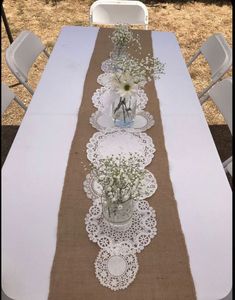 the table is decorated with white flowers and doily on burlap runneres