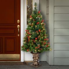 a small christmas tree sitting on top of a metal planter in front of a door