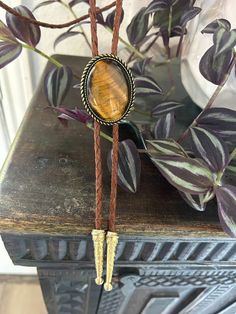 a close up of a piece of jewelry on a table with plants in the background