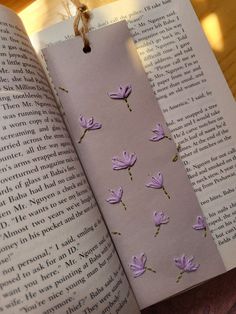 an open book with purple flowers on it sitting on a table next to a string