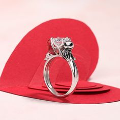 a silver ring with two skulls on it sitting on top of a red heart shaped napkin