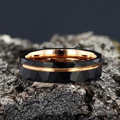 a black and gold wedding ring sitting on top of a rocky surface with rocks in the background