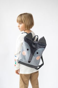 a young boy wearing a backpack with a fox design on it's back pocket