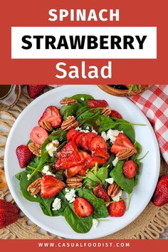 spinach strawberry salad on a white plate with strawberries and pecans in the background