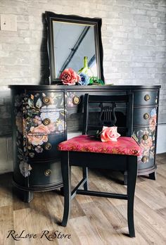 a black dresser with flowers painted on it and a pink chair in front of it