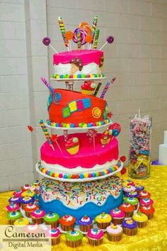 a multi layer cake with candy and candies on the top is surrounded by cupcakes