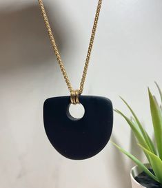 a black and gold necklace with a white circle hanging from it's center, next to a potted plant